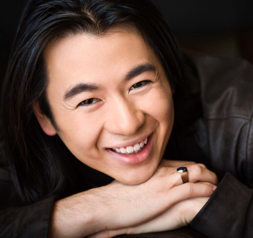 Kevin smiles brightly as he rests his chin on his hands.